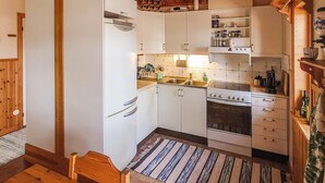 Een compacte keuken met witte kasten, een ingebouwde oven en een kookplaat. Er staat een houten eettafel met een gestreepte tafelkleed.