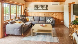Een gezellige woonkamer met een hoekbank, een bijzettafeltje en een televisie aan een houten wand.