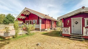Een rode houten woning met een veranda en een kleine tuin.