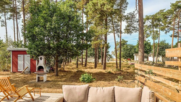 Een houten terras met een beige bank en twee houten stoelen.