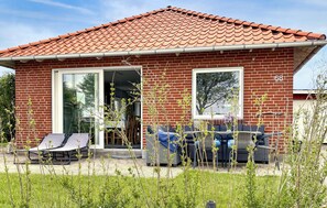A red brick house with a tiled roof, a glass door, and a patio with outdoor furniture.