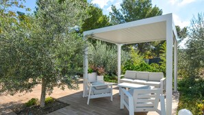 Et overdækket udendørs opholdsområde med hvide møbler og et pergola.
