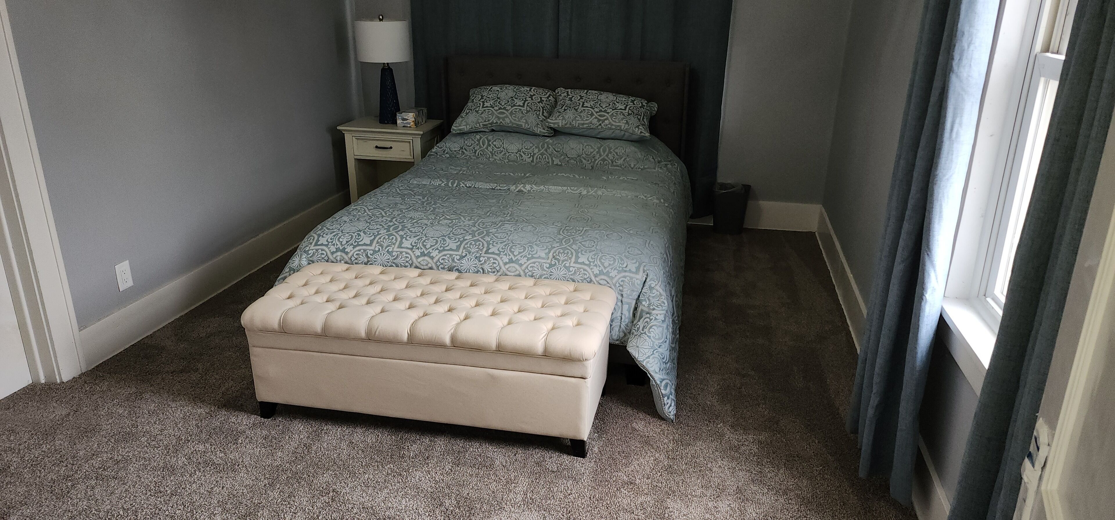 A bedroom with a bed, a nightstand, a lamp, and a window.