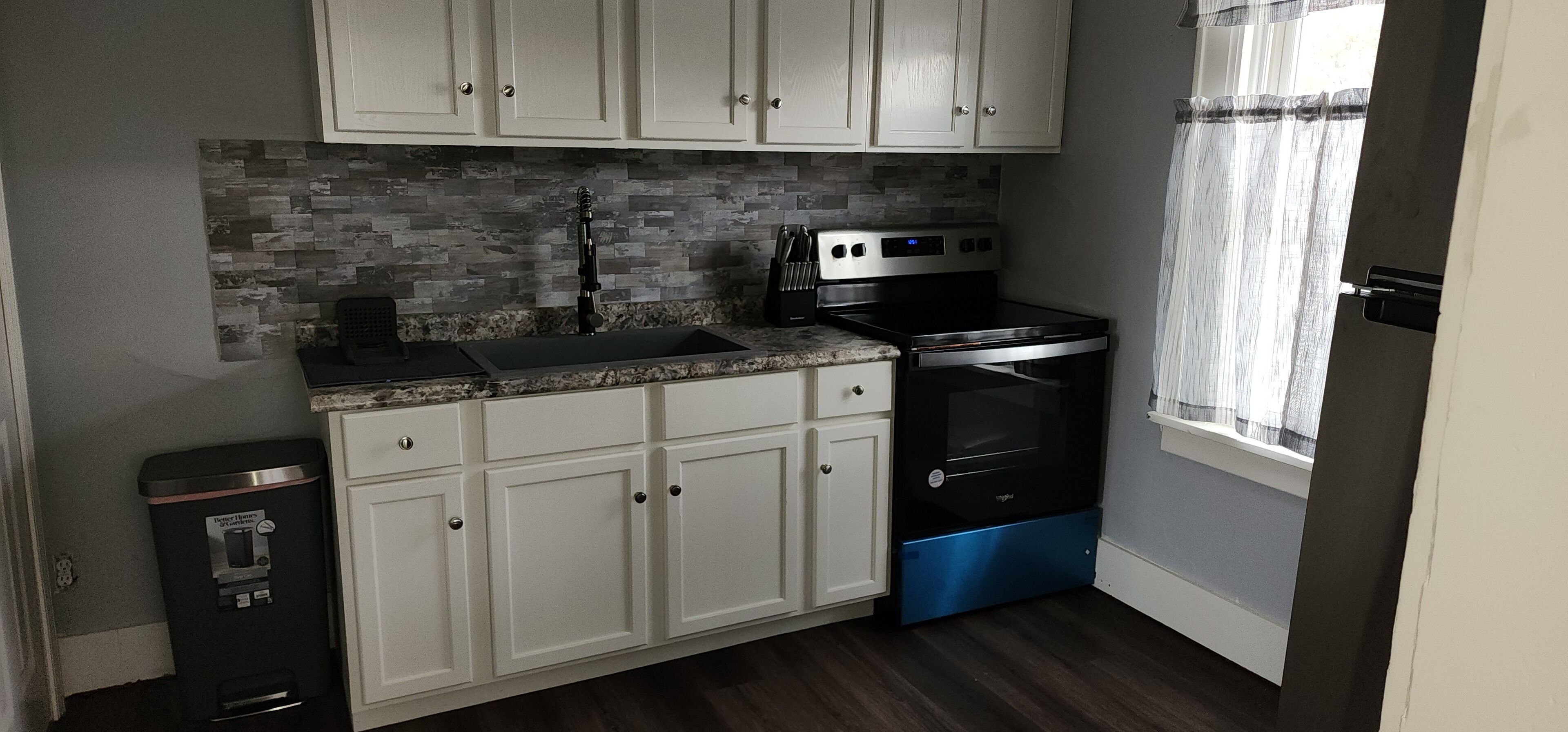 A compact kitchen with white cabinets, a black stove, and a stainless steel sink.