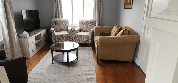 A living room with a sofa, two armchairs, a coffee table, a TV, and a window with curtains. - Great location Close to downtown, interstate, zoo, UNO, UNMC, Shopping and more. (Omaha)