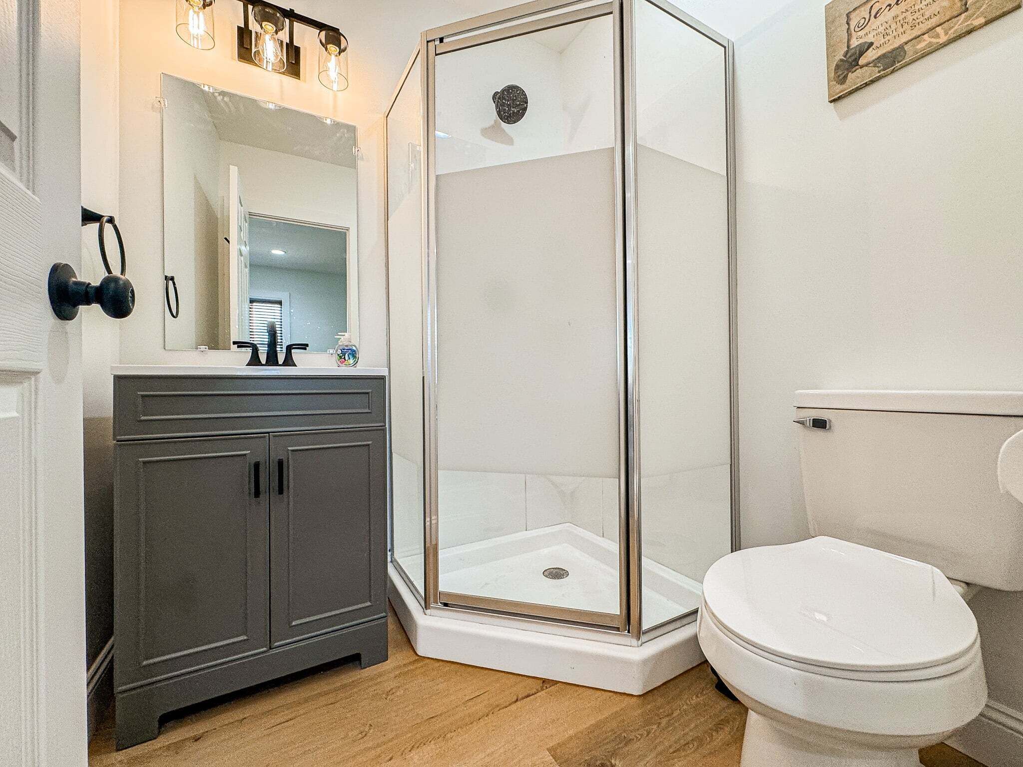 A bathroom with a shower, toilet, vanity, and a mirror.