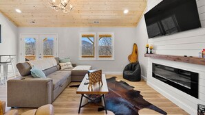 Una sala de estar moderna con techo de madera, chimenea, sofá, mesa y alfombra de cuero de vaca.