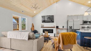 Una sala de estar moderna con sofá, una butaca, chimenea y una zona de cocina con electrodomésticos.