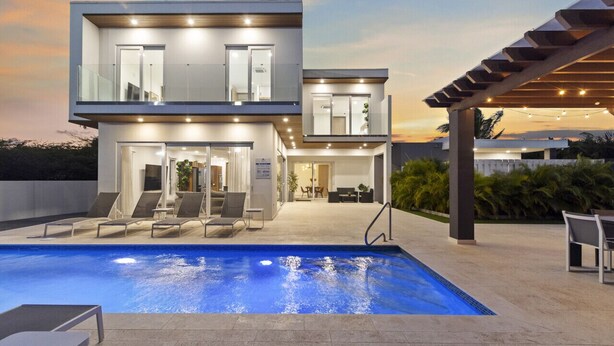 Ein modernes, zweistöckiges Gebäude mit Schwimmbad, Außenbereich mit Sitzgelegenheiten und einer überdachten Terrasse.