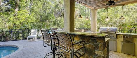 An outdoor bar area with a pool, bar stools, and a grill.
