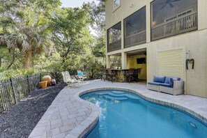A swimming pool with a stone deck, outdoor seating, and a covered patio area.