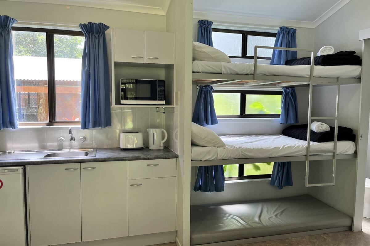 A bunk bed room with a kitchen area including a microwave, toaster, and kettle.