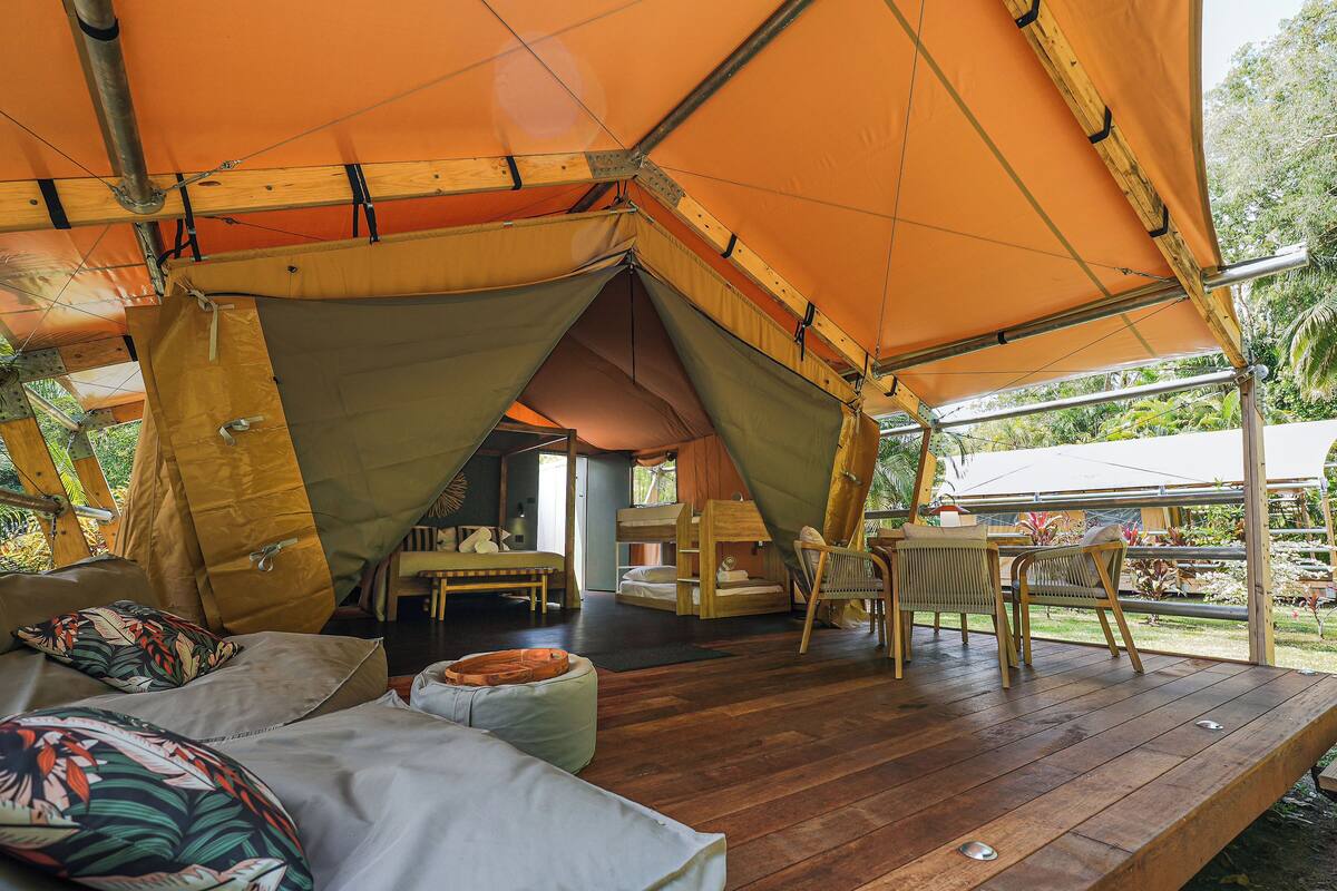 A tented accommodation with a wooden deck, a dining area, and a bed with a pillow.