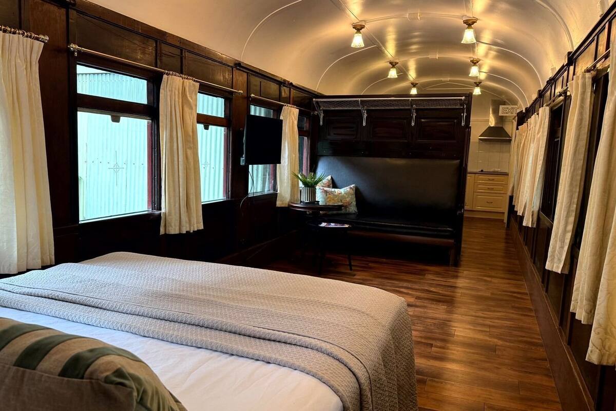 A train bedroom with a large bed, a small table with a plant, and curtains on the windows.