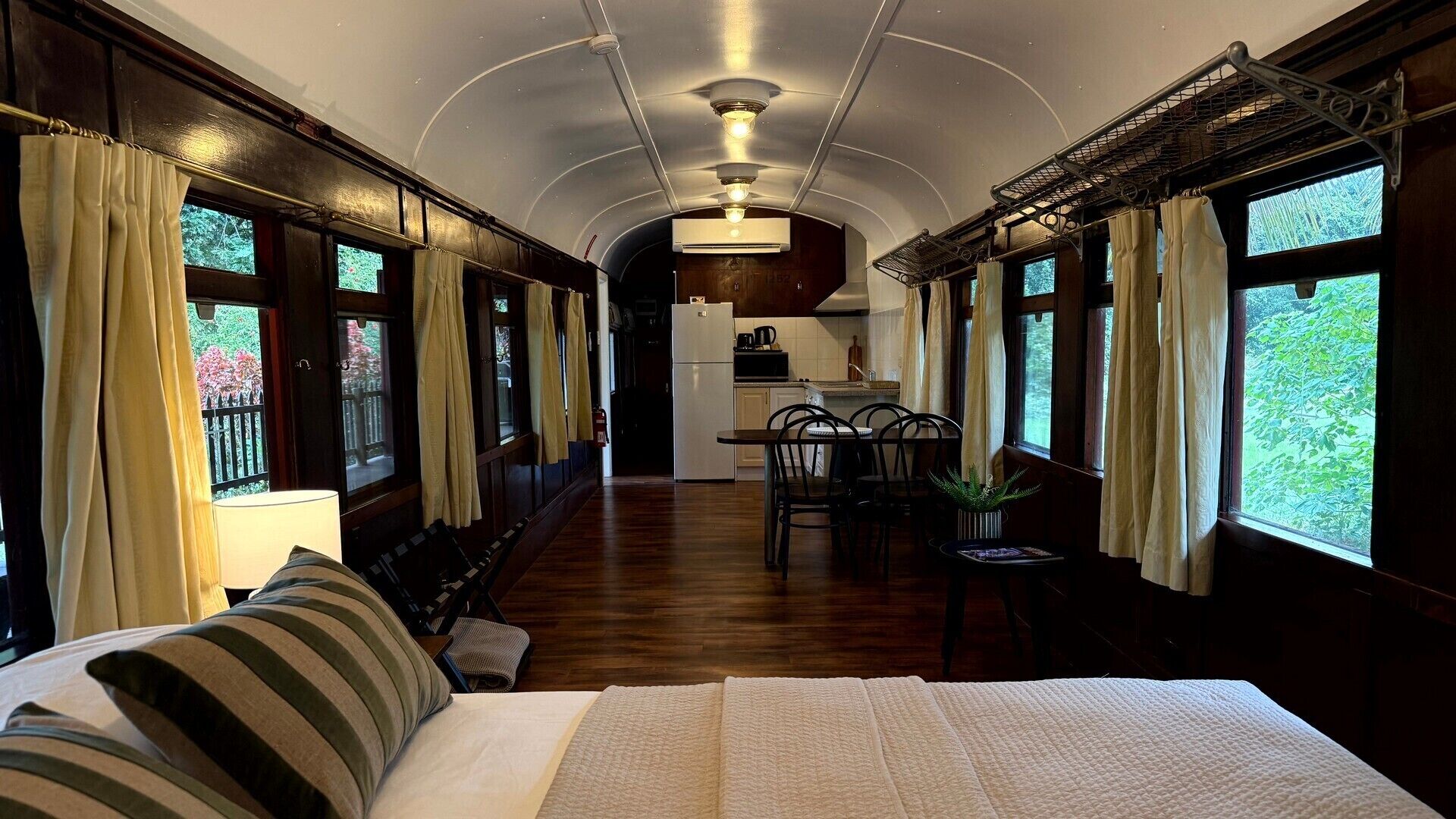 Un compartiment de train aménagé en chambre à coucher, avec un lit, une petite table et un coin cuisine à l’arrière-plan.