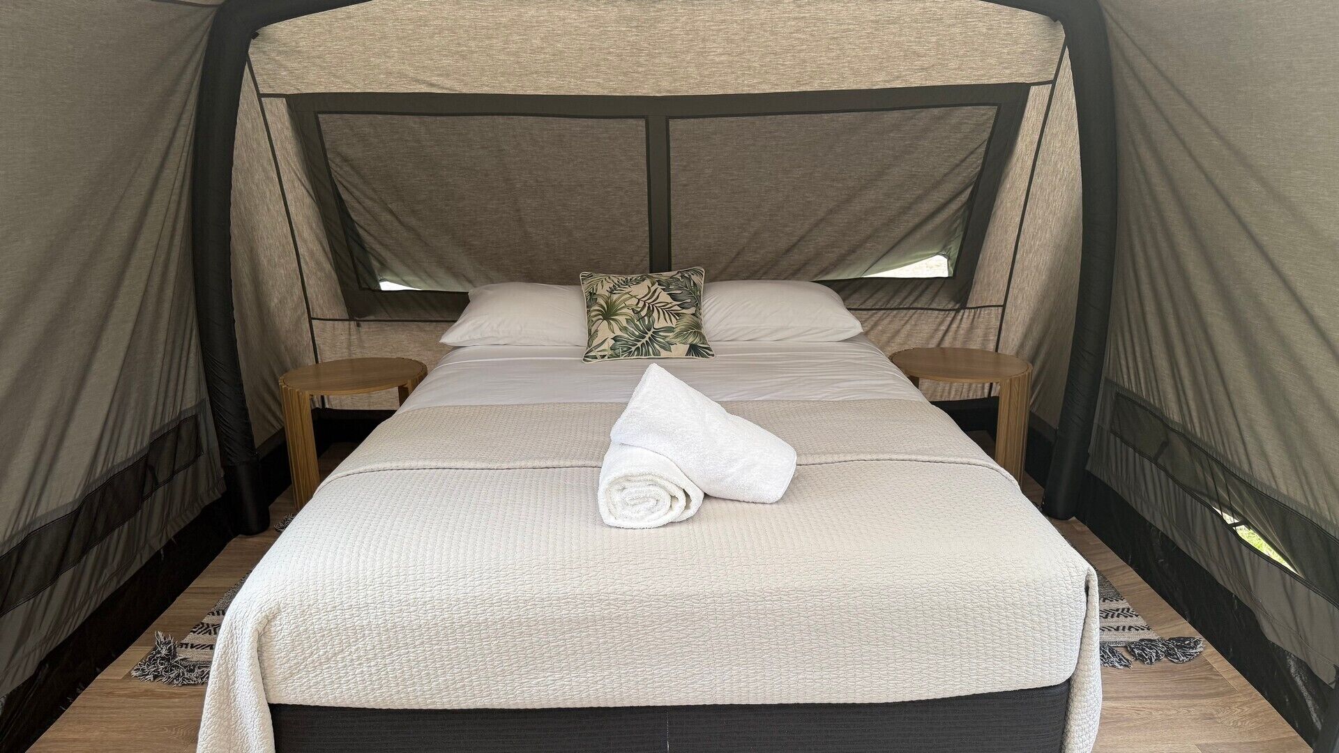 A single bed with a canopy, two wooden nightstands, a rolled white towel, and a patterned pillow.