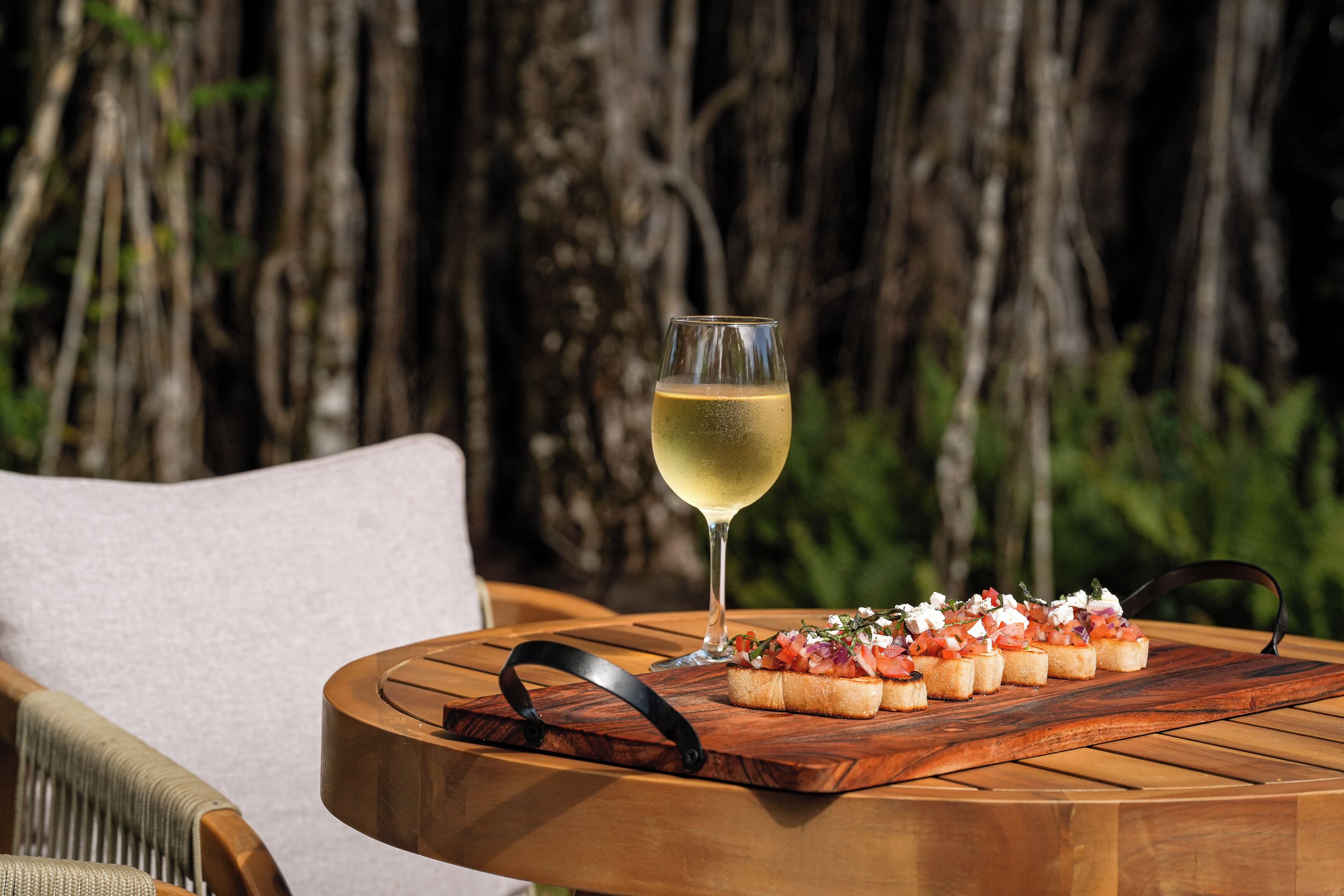 A round wooden table with a glass of white wine and a wooden board with appetizers.