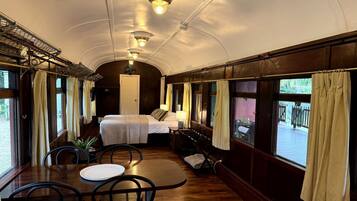 Un vagón de tren con cama, mesa, sillas y amplias ventanas.