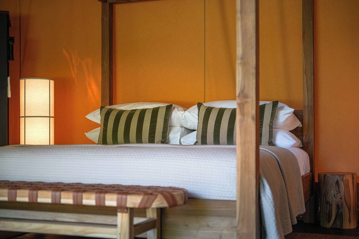 A bed with striped pillows, a bedside lamp, and a wooden bench.