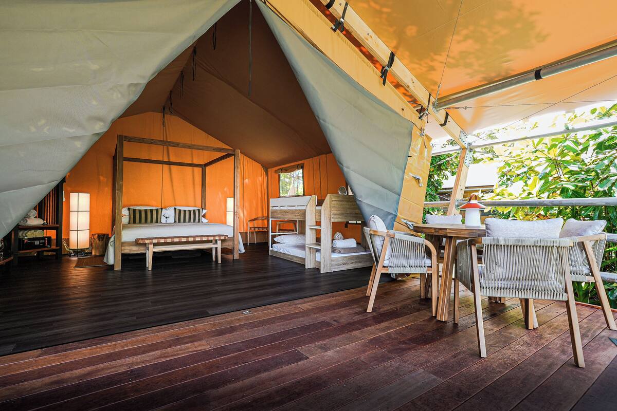 A cozy tented accommodation with a wooden floor, a bed, a table, and chairs.