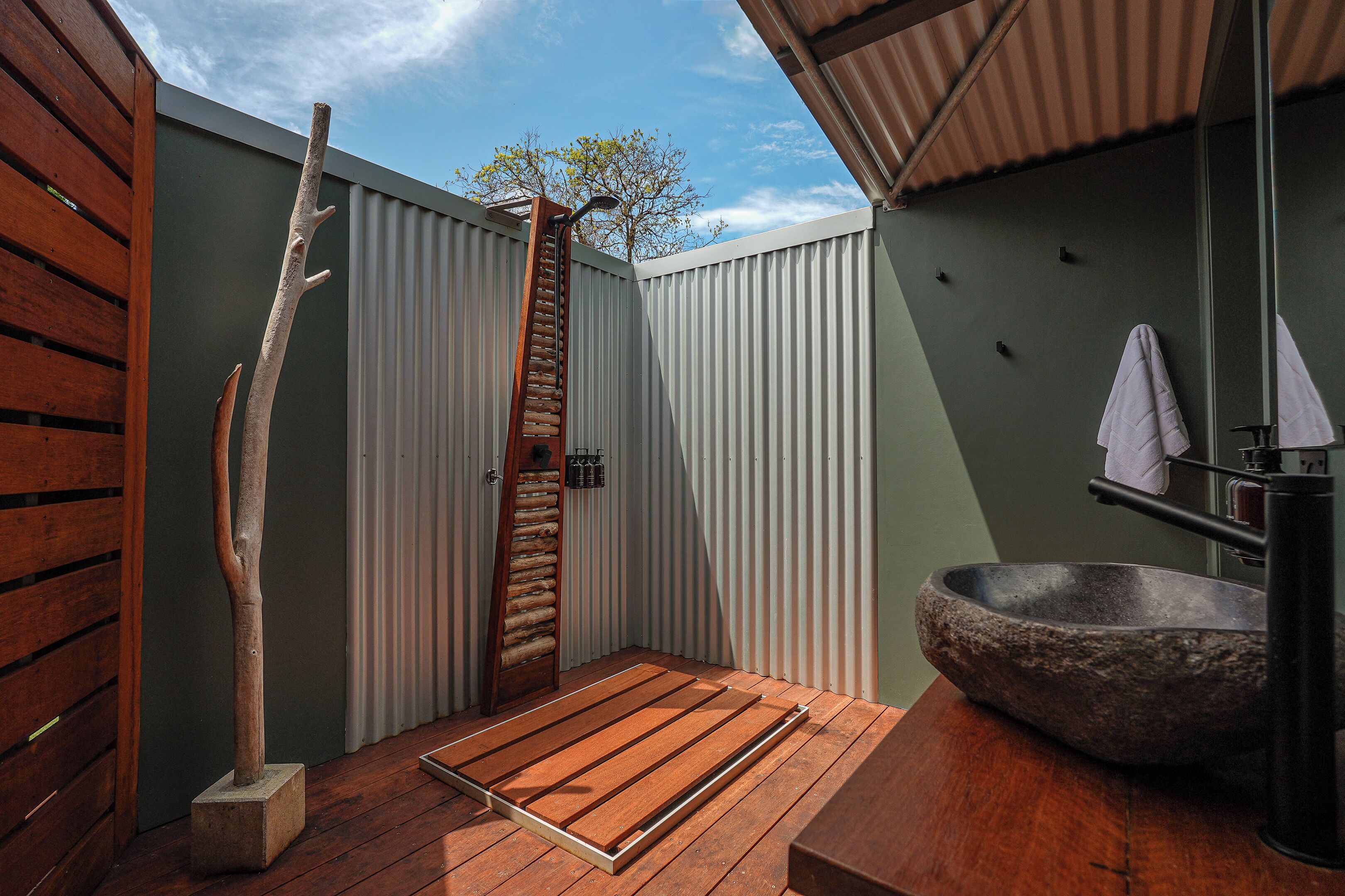 A modern bathroom with a wooden deck, a stone sink, and a wooden door.