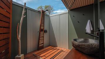 A modern bathroom with a wooden deck, a stone sink, and a wooden door.