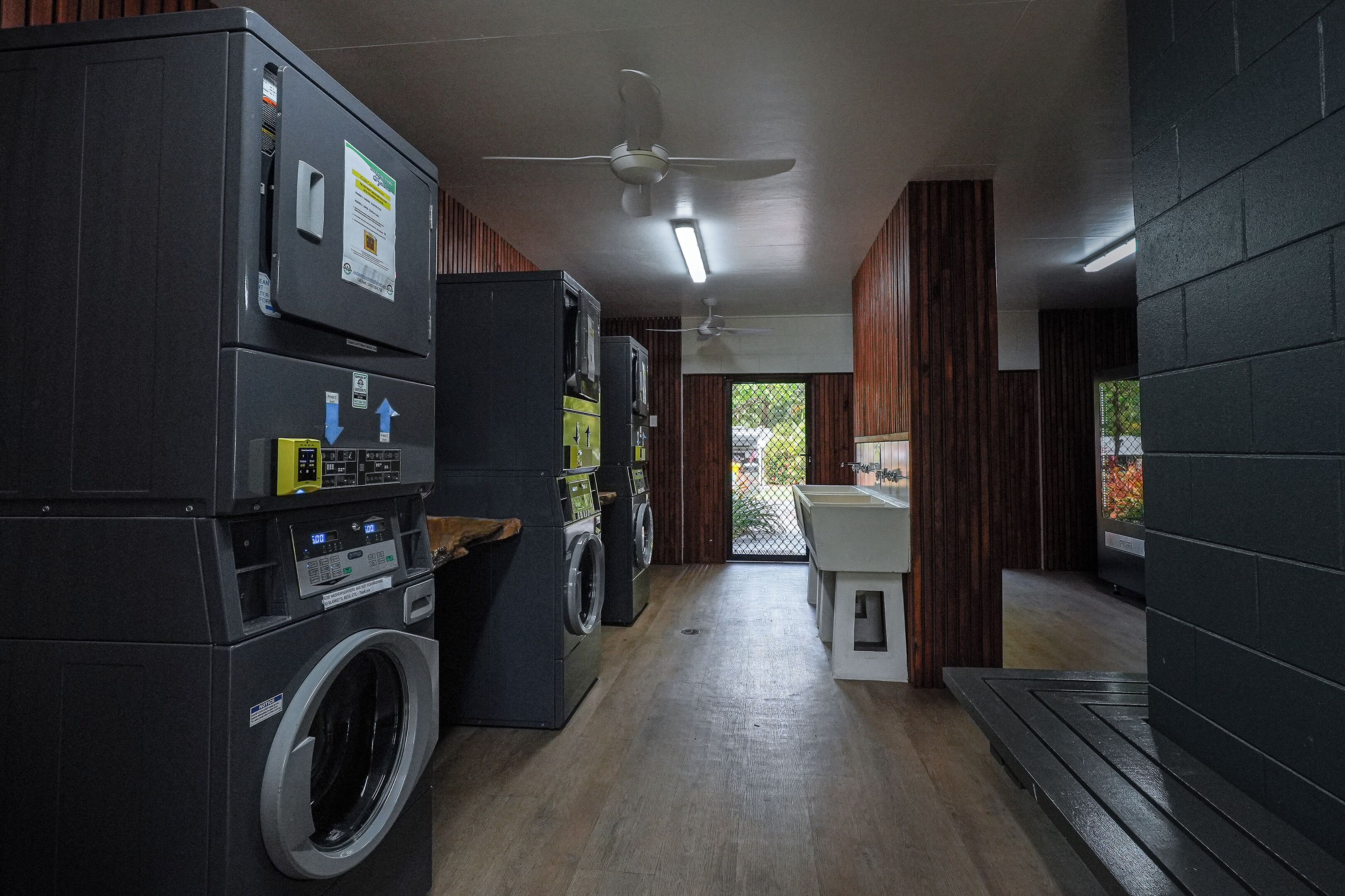A laundry room with stacked washers and dryers, a ceiling fan, and a view of the outside through a door.