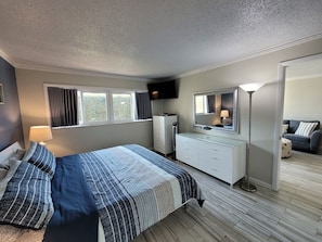 Une chambre à coucher avec un lit, une commode, un miroir et un téléviseur fixé au mur.