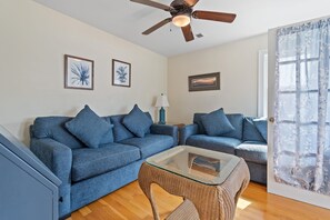 A living room with two sofas, a glass coffee table, a ceiling fan, and framed artwork on the walls. - "A Perfect Landing" is a 6 Bedroom / 6.5 Bath Home w/ Private Pool & Elevator. (Holden Beach)