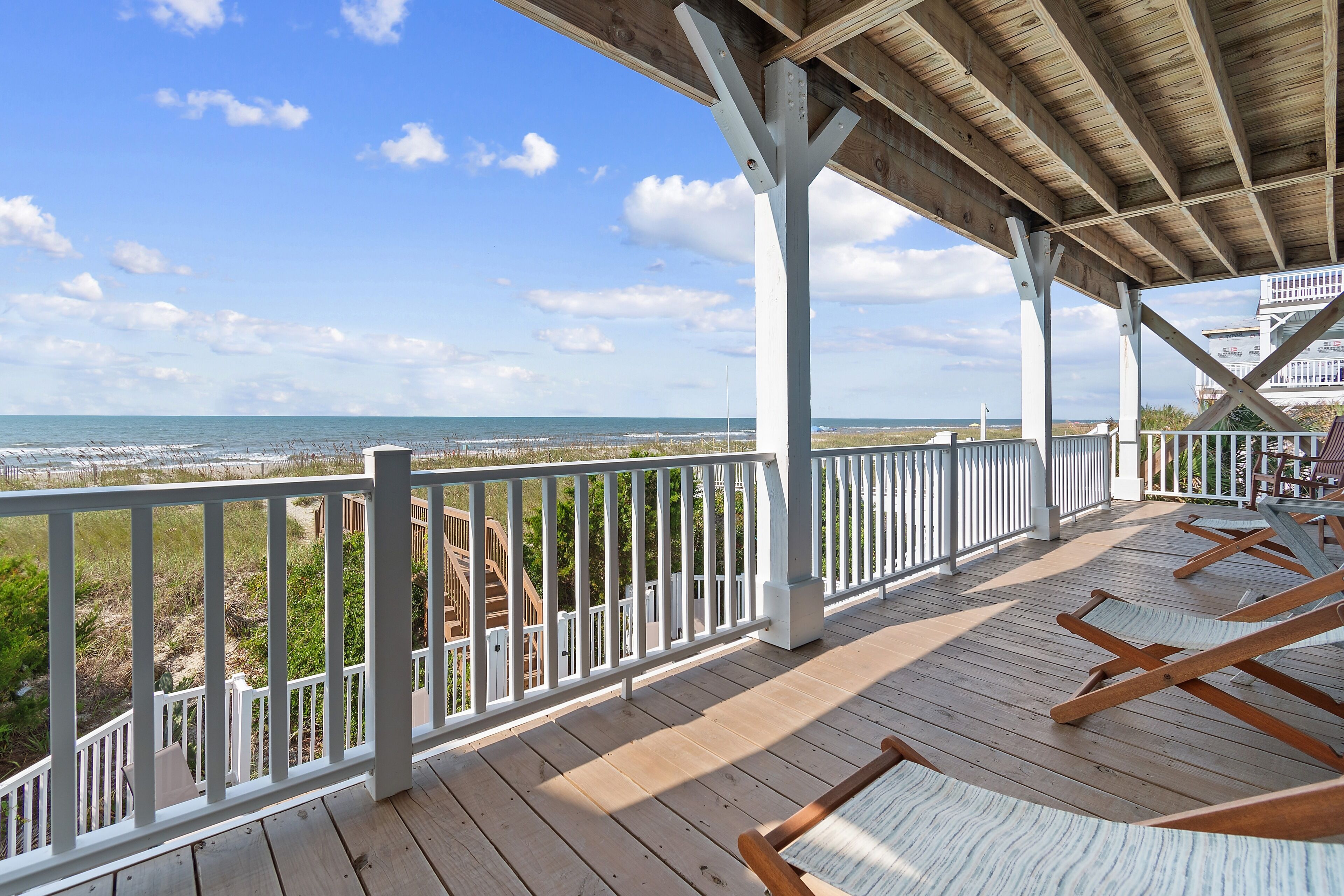 A wooden deck with white railings overlooking a beach and ocean.