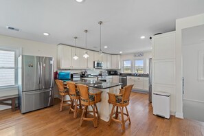 A modern kitchen with stainless steel appliances, a central island with bar stools, and pendant lighting. - "A Perfect Landing" is a 6 Bedroom / 6.5 Bath Home w/ Private Pool & Elevator. (Holden Beach)