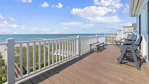 En træterrasse med gelænder i hvidt, der vender ud mod en strand.