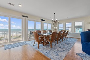 A dining room with a view of the beach, featuring a large table with chairs, a chandelier, and a view of the ocean. - "A Perfect Landing" is a 6 Bedroom / 6.5 Bath Home w/ Private Pool & Elevator. (Holden Beach)