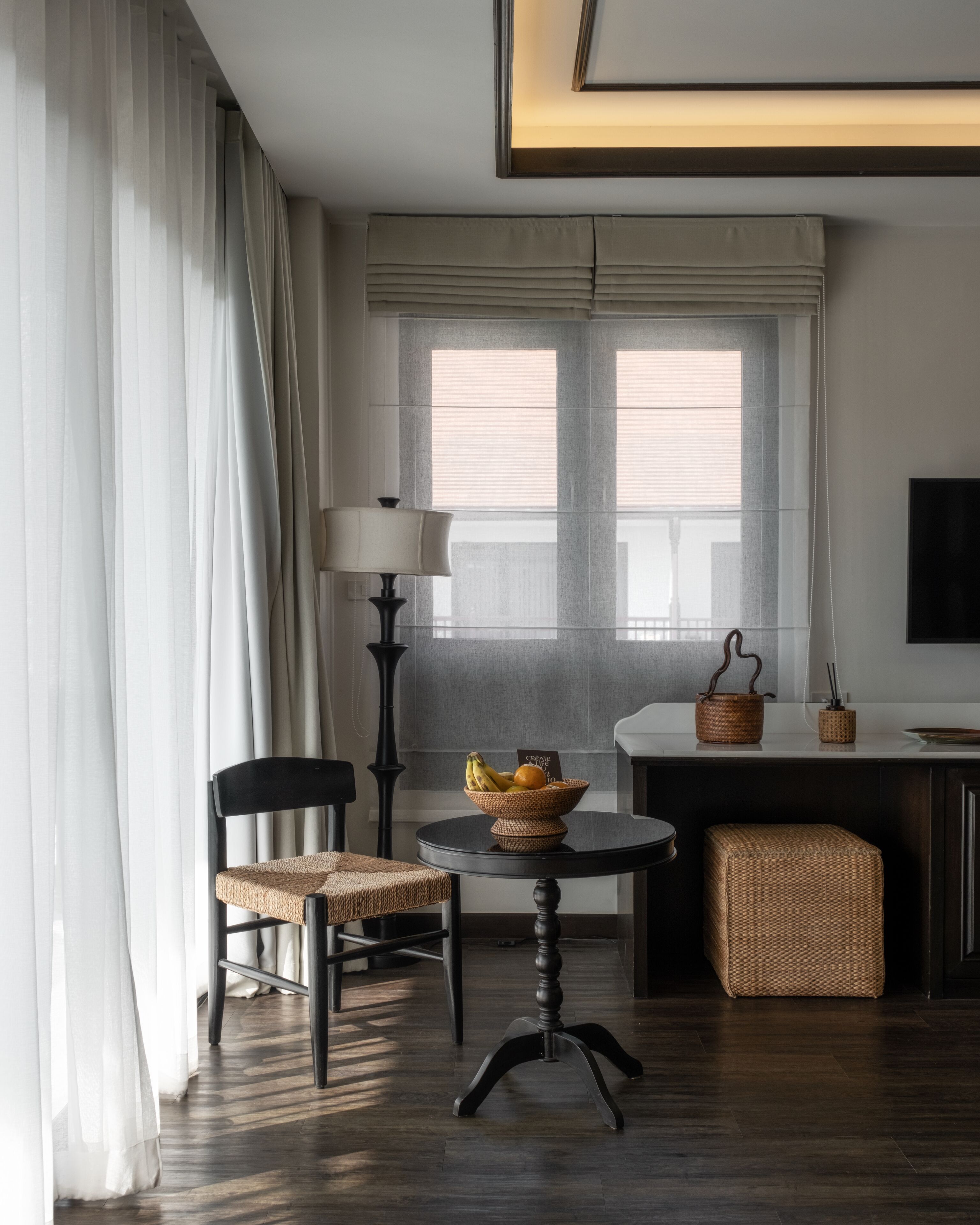 Una habitación moderna con una mesa de comedor, sillas, una lámpara, una cesta de fruta y un televisor en la pared.