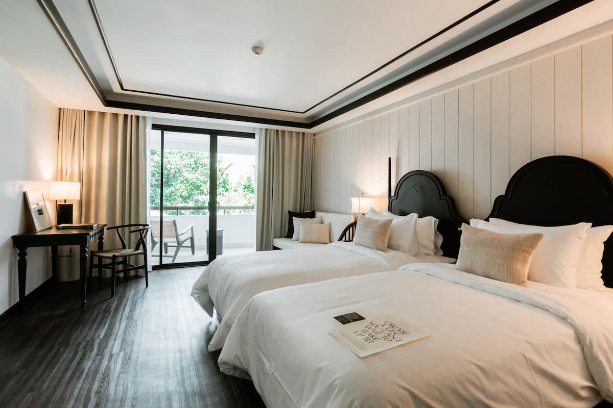 Quarto de hotel com duas camas, uma escrivaninha e uma cadeira.