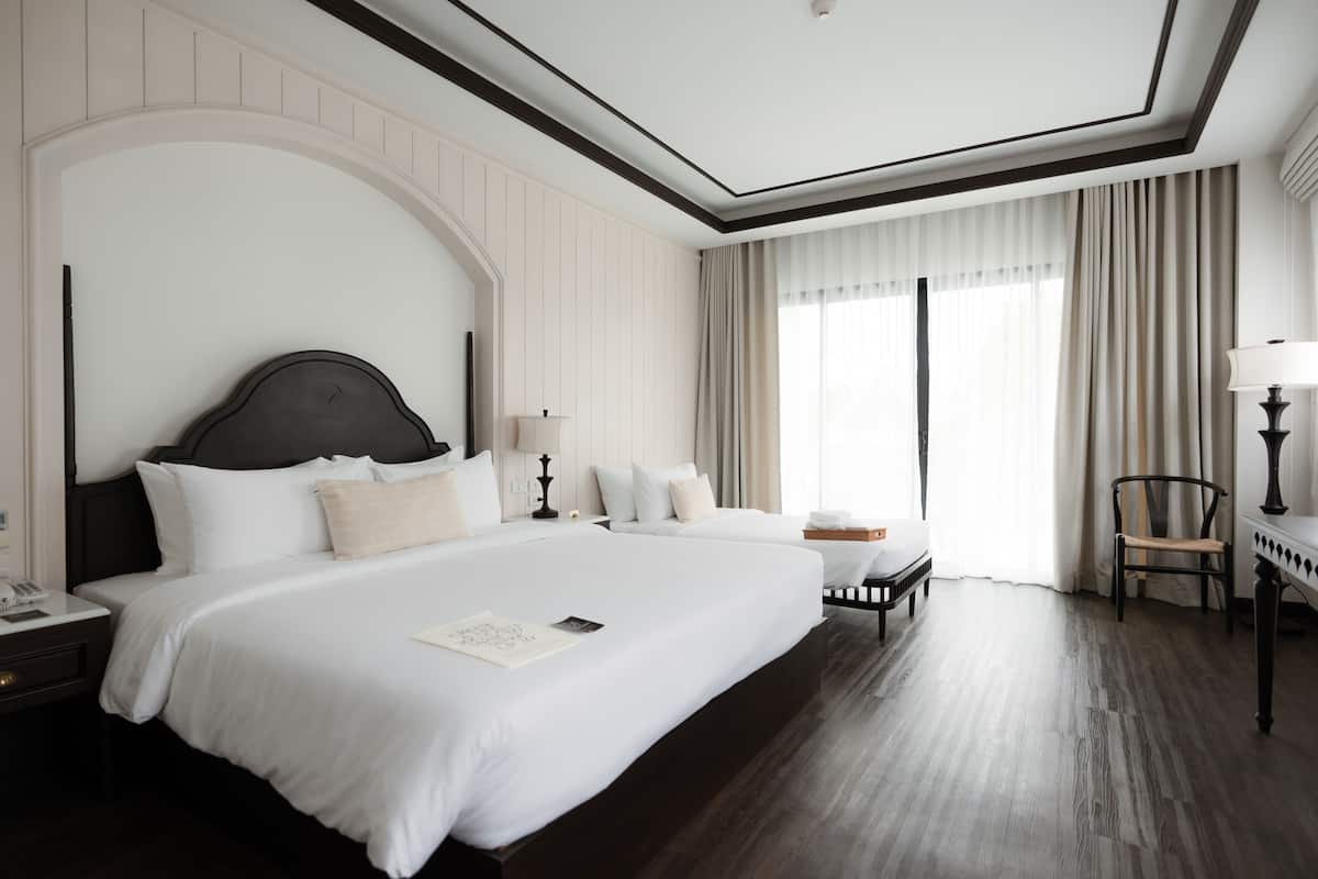Quarto de hotel com uma cama grande, mesa de cabeceira, cadeira e escrivaninha com abajur.