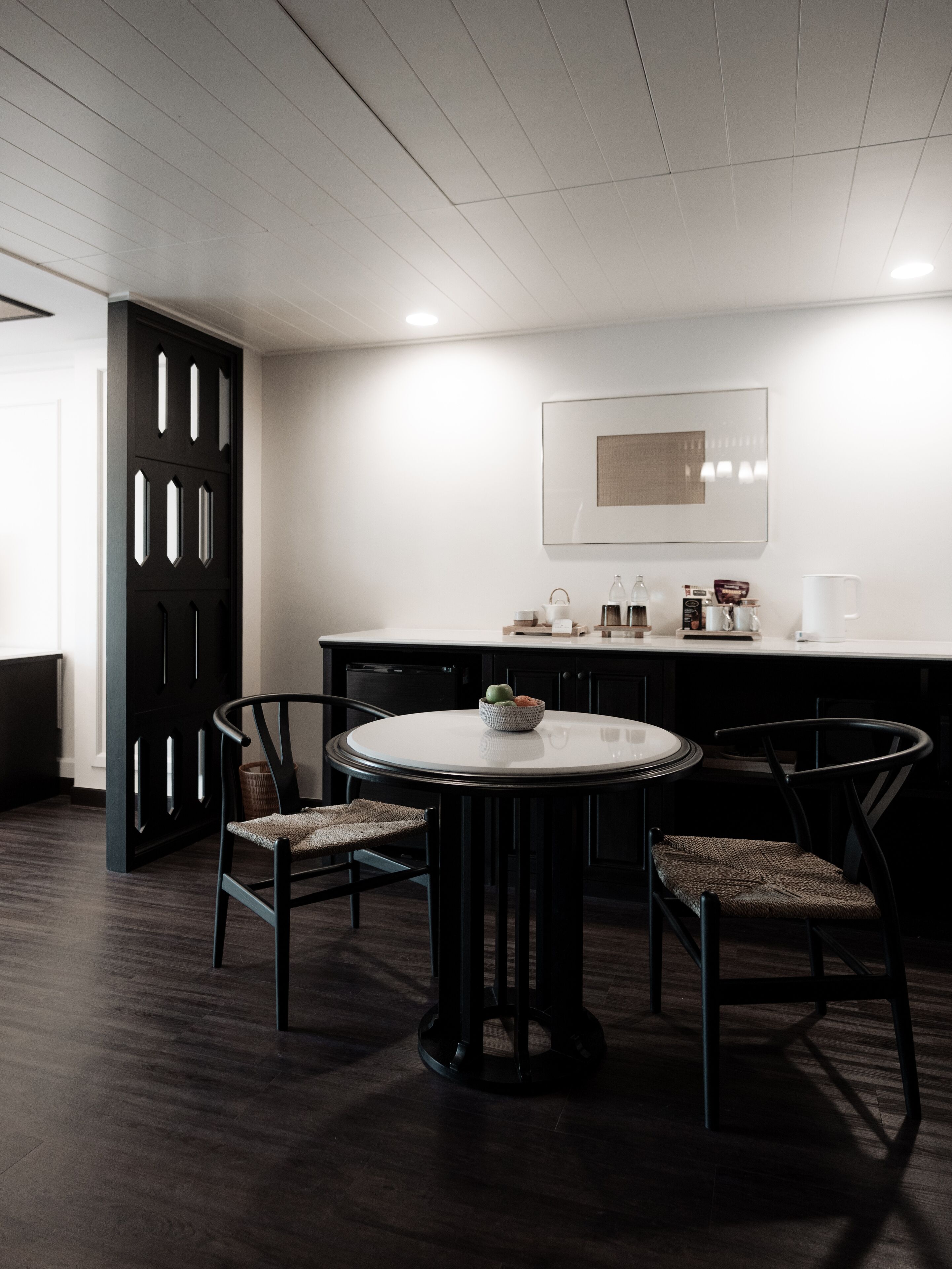 Un comedor moderno con una mesa redonda, cuatro sillas, una puerta negra y una pared blanca con un cuadro enmarcado.
