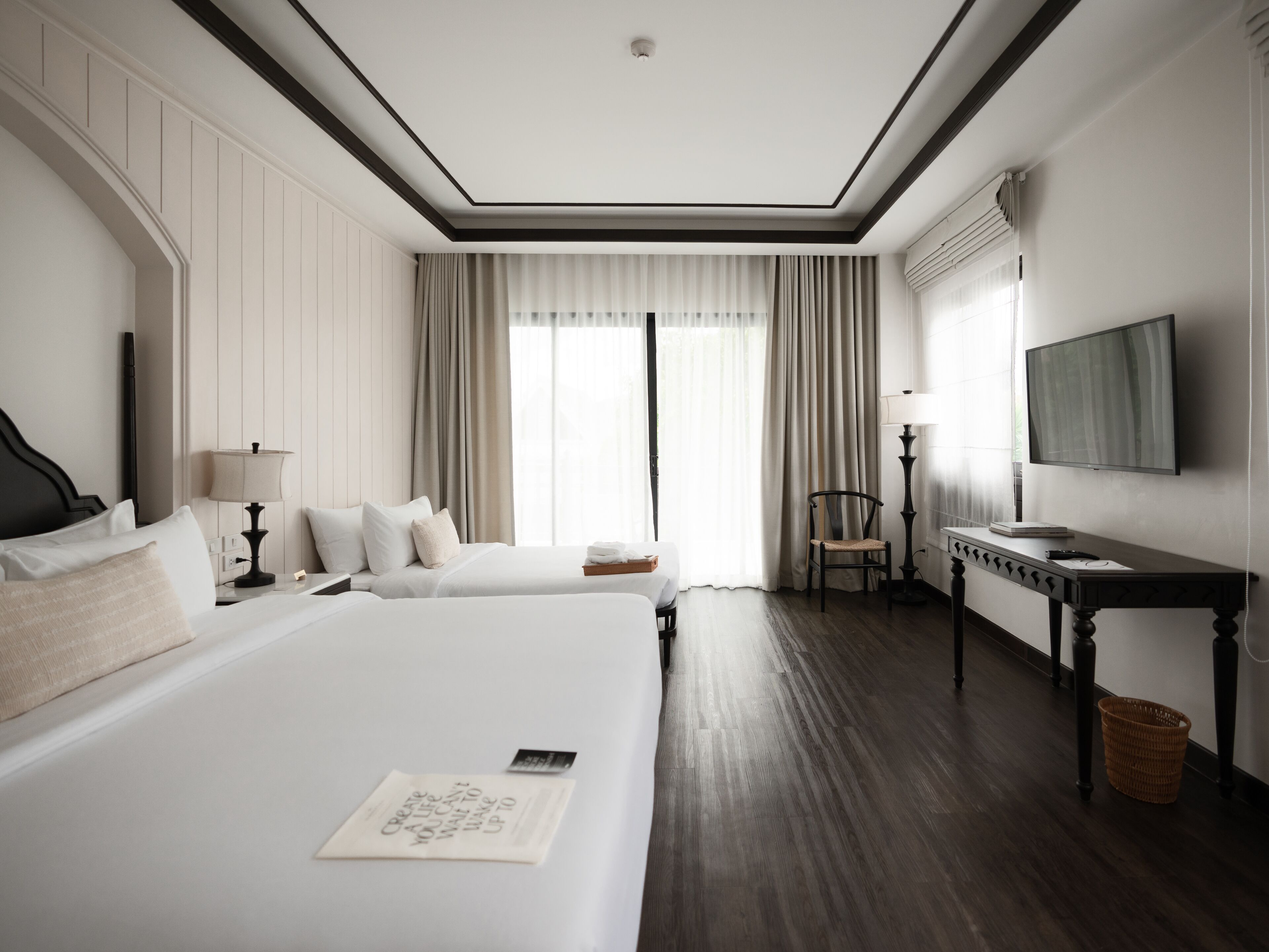 A hotel room with two beds, a desk, a chair, a TV, and a window with curtains.