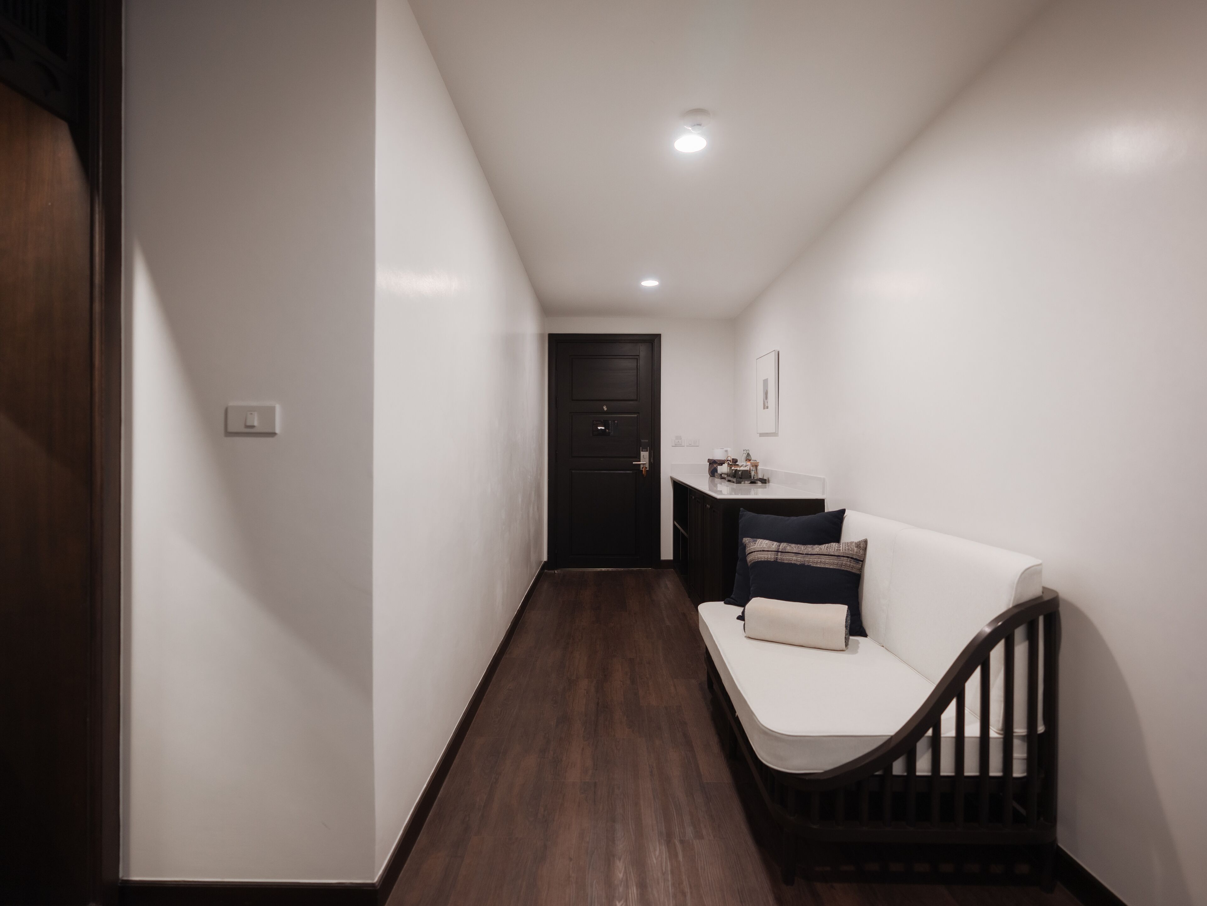 A narrow hallway with a dark wooden floor, a white wall, and a black door at the end.
