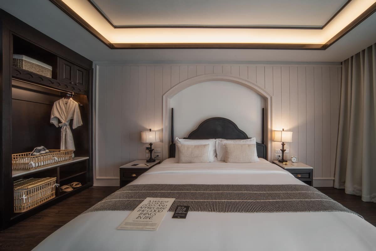 Quarto de hotel com uma cama grande, duas mesas de cabeceira com abajures, um guarda-roupa e uma cabeceira.
