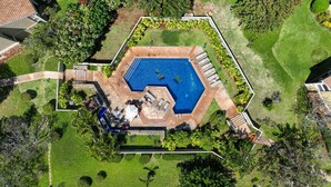 An aerial view of a swimming pool surrounded by a garden with a patio area.