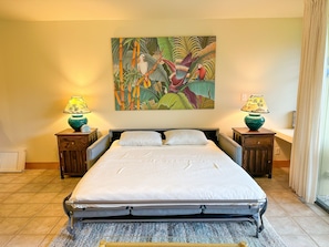 A bedroom with a bed, two nightstands, two lamps, a painting, and a window with curtains. - Turtle Bay Creek view - 1Bed 2Bath Kuilima Condo - Sleeps 4 (Kahuku)