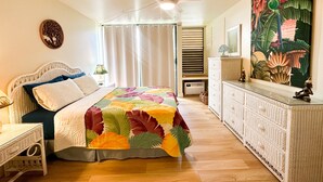 A bedroom with a bed, a nightstand, a dresser, a ceiling fan, a window with curtains, and a wall painting.