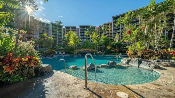 A hotel with a swimming pool surrounded by tropical plants and palm trees.