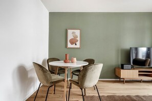 A modern living room with a round table, two chairs, a television, and a framed artwork on the wall.