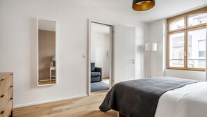 Une chambre à coucher comprenant un lit, une armoire, un miroir et une porte donnant sur une autre pièce.