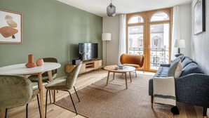 Un salon moderne comprenant un coin repas, un canapé, un téléviseur et un balcon offrant une vue sur les immeubles.