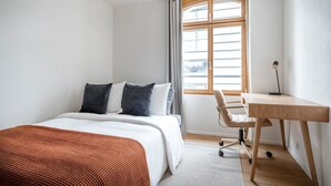 A modern hotel room with a bed, a desk, and a window.