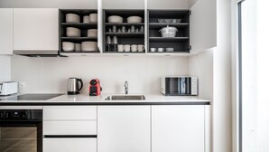 A modern kitchen with white cabinets, a stainless steel sink, a kettle, a toaster, and a microwave.
