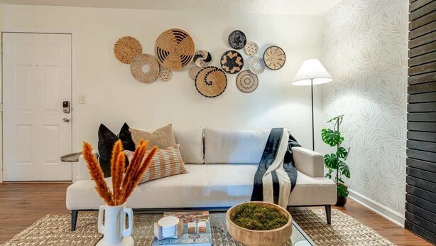Una sala de estar con un sofá blanco, decoración en la pared, una mesita de centro con libros y un cuenco, y una lámpara.